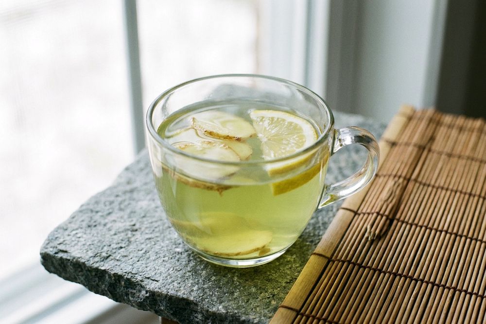 Clear cup of green tea with ginger slices and a lemon wedge