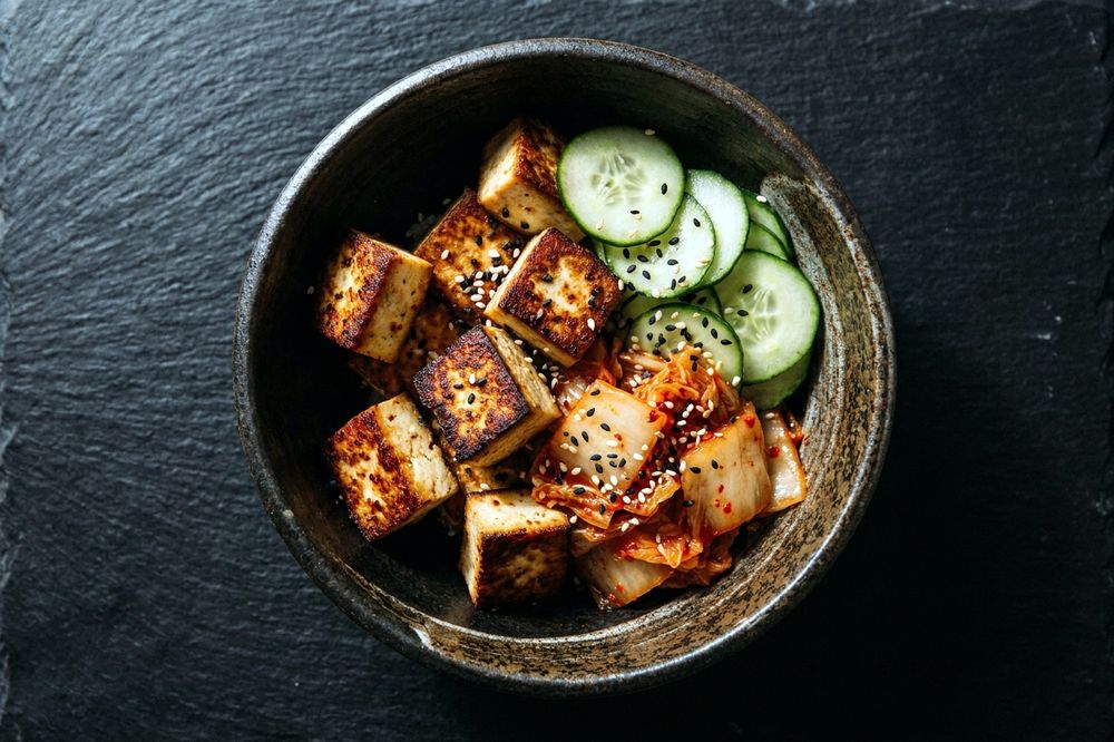 Bowl of tofu cubes with red kimchi, cucumber and sesame seeds