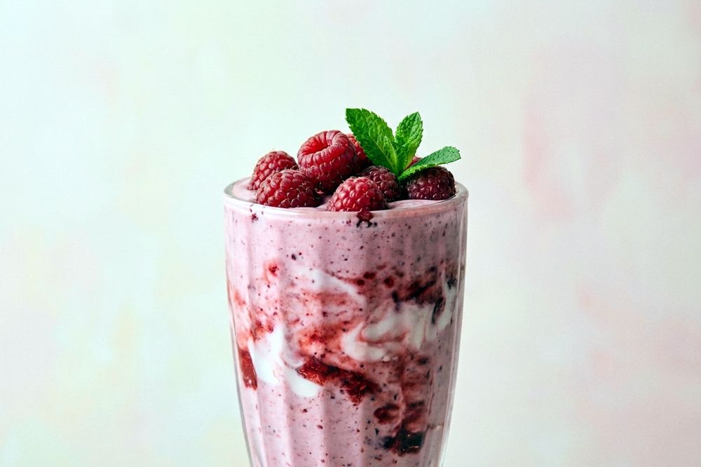 Glass of pink berry lassi topped with a few whole raspberries