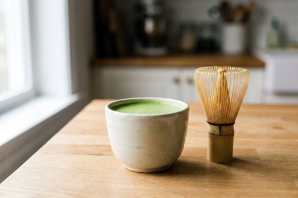 Bright green matcha latte in a ceramic cup with a bamboo whisk beside it