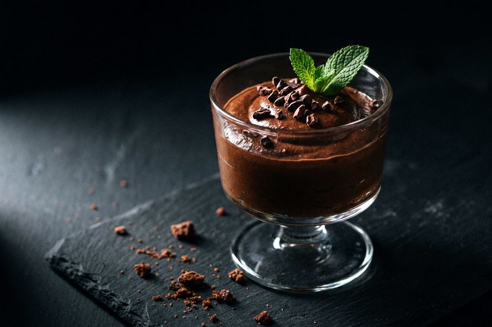Small glass of dark chocolate mousse topped with cocoa nibs and a mint leaf