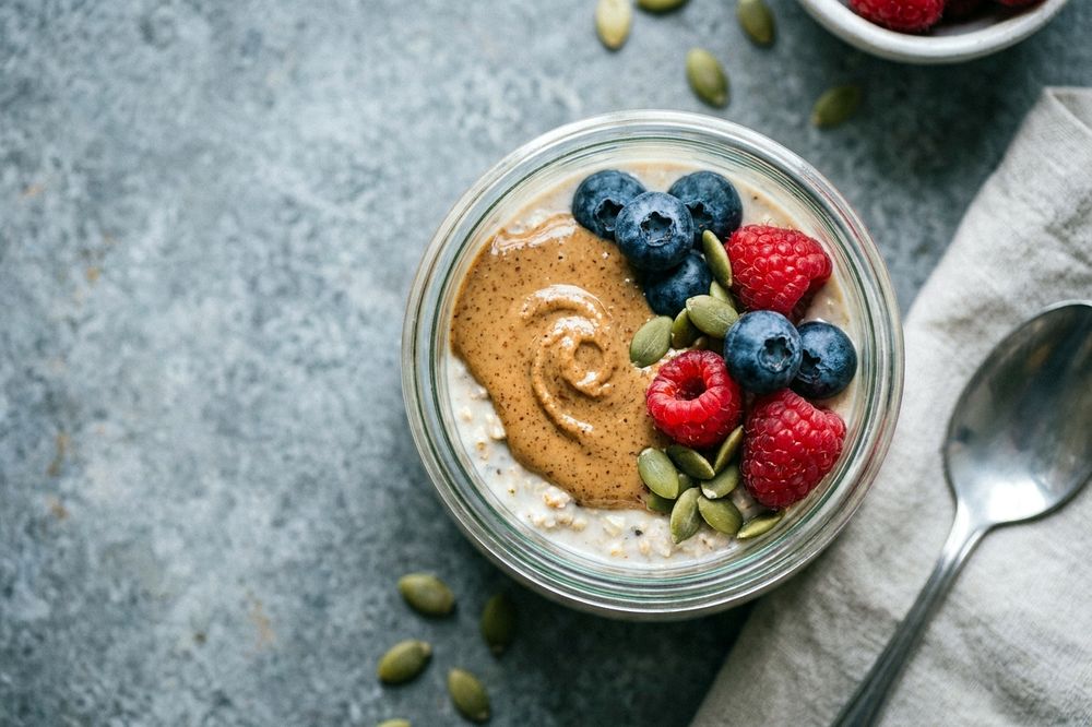Jar of overnight oats topped with almond butter, berries and seeds