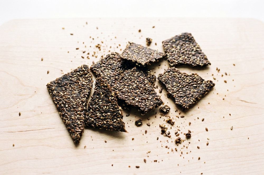 Thin seeded crackers broken into pieces on a wooden board